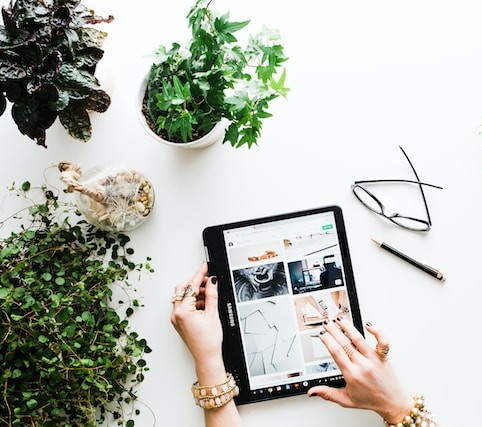 Woman browsing design content on tablet with plants around her